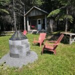 a fire pit in a yard with chairs and a wood cabin in the background