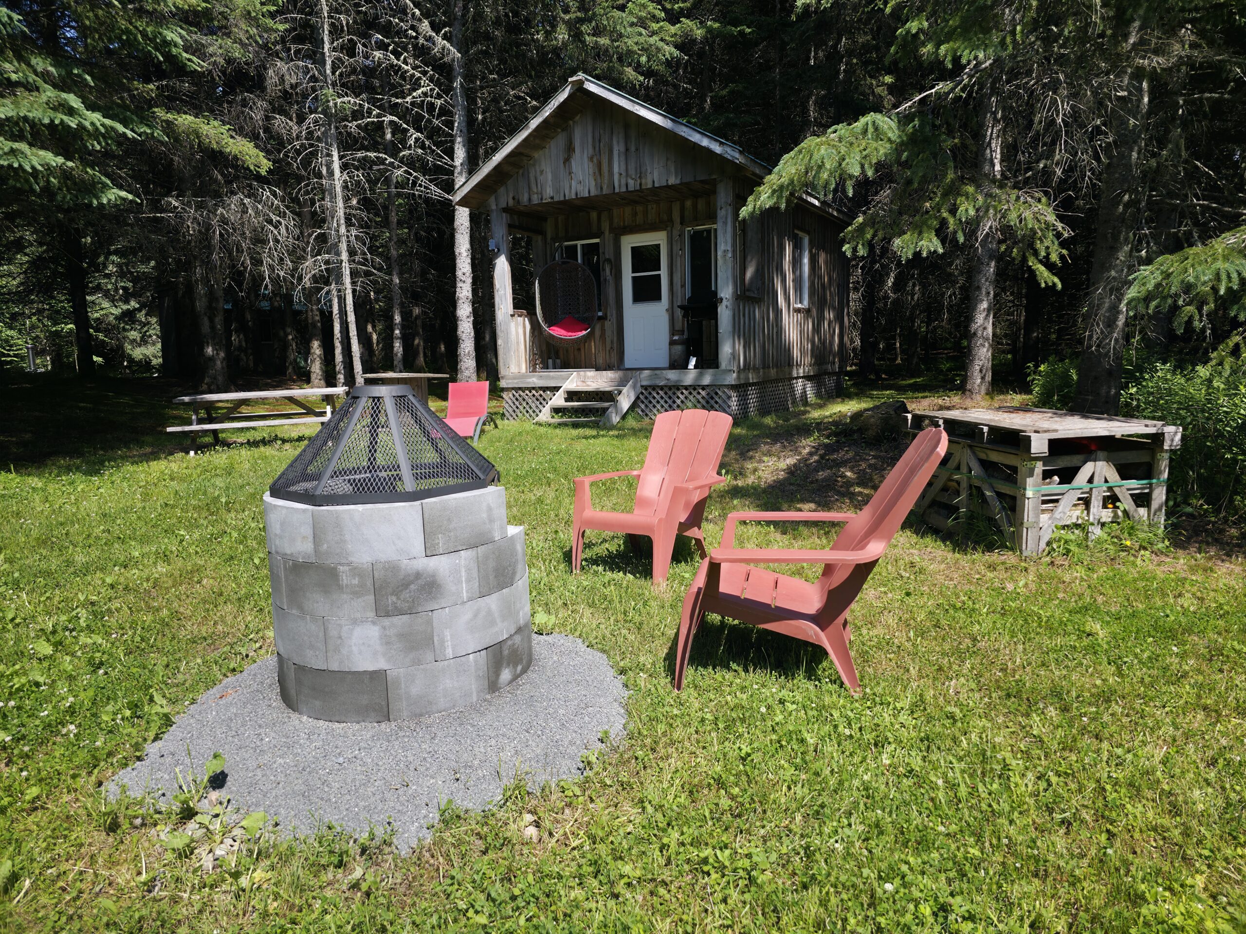 a fire pit in a yard with chairs and a wood cabin in the background
